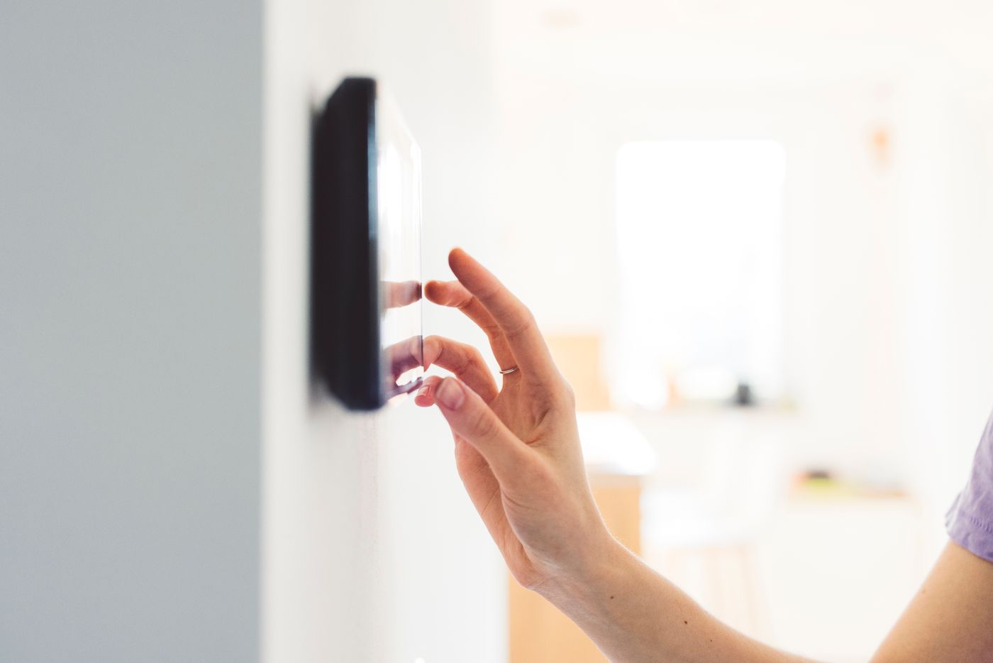 Close-up of a woman's hand touching a smart home security panel.