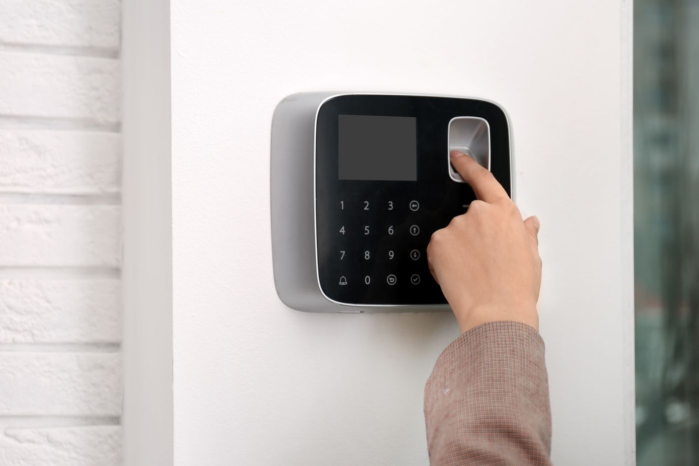 Businesswoman scanning finger on alarm system keypad.