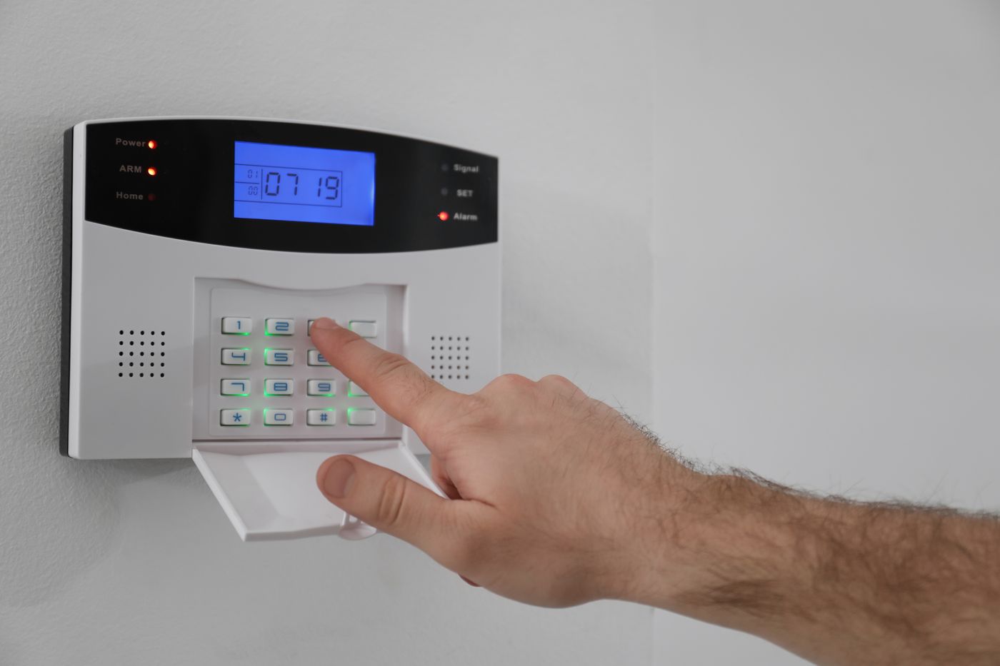 Man entering security code on alarm keypad for access control.