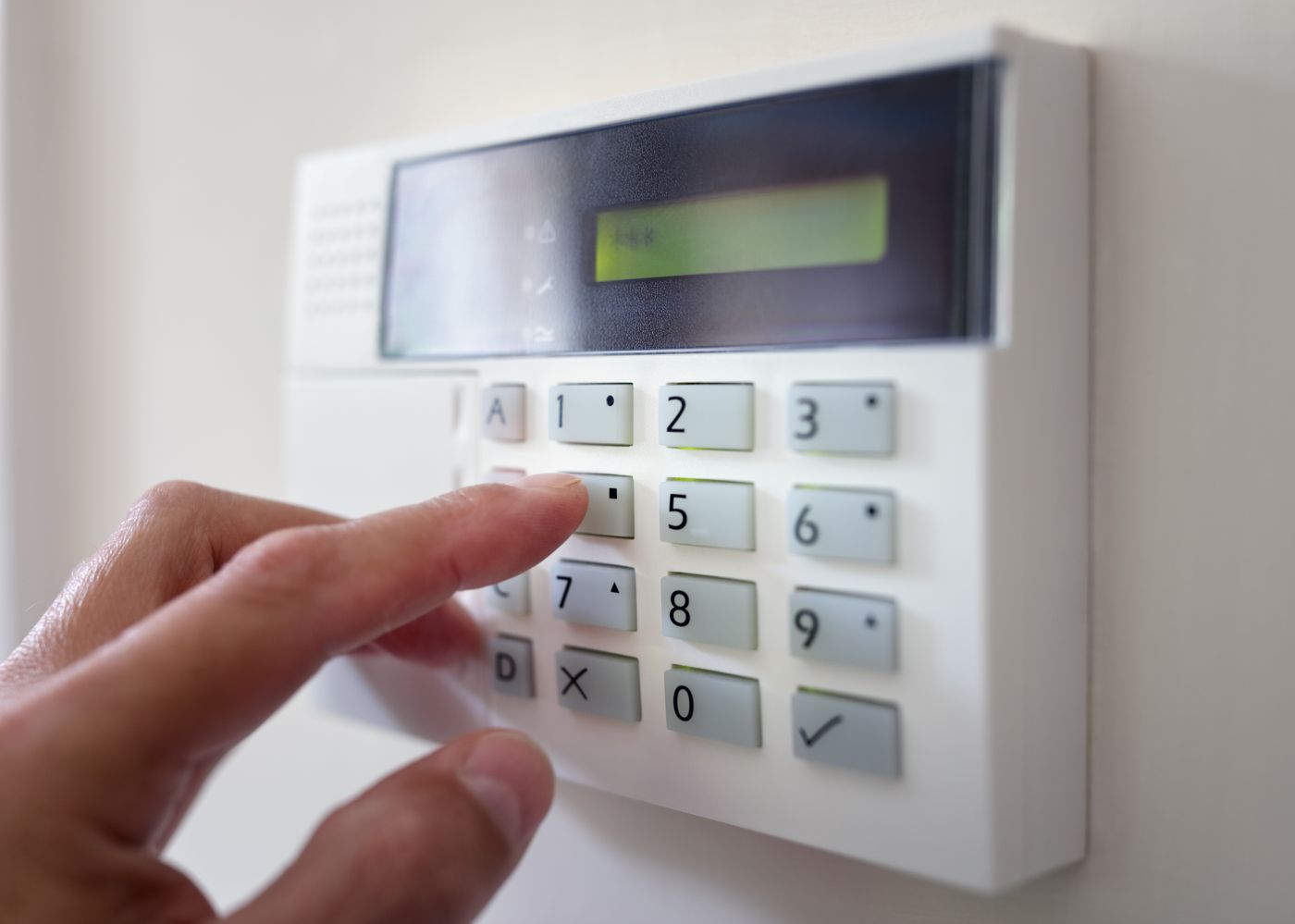 Person entering code on electronic security keypad for home or office alarm system access control.